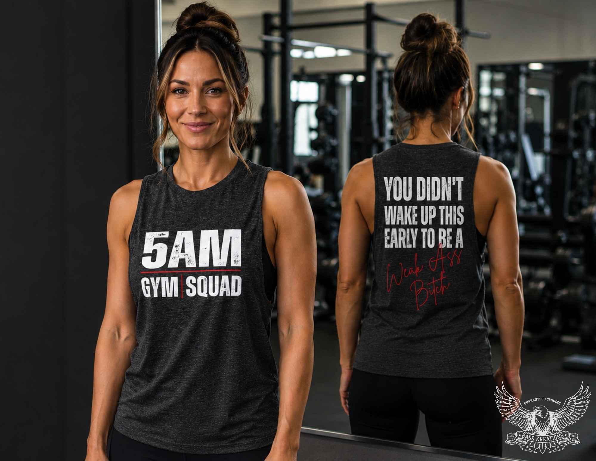 A woman in a gym wearing a dark heather gray sleeveless tank top with white text reading '5AM GYM SQUAD' on the front, and the back text 'YOU DIDN'T WAKE UP THIS EARLY TO BE A Week ass bitch ' in white and red script. She is shown facing forward and reflected in a mirror showing the back design.