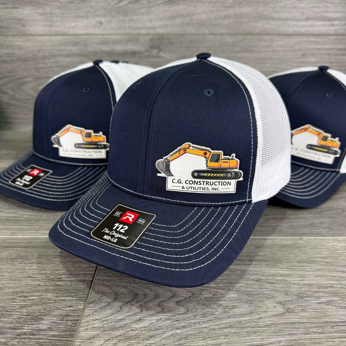Navy and white Richardson 112 trucker hats with a full color UV printed patch showing a construction company's excavator logo